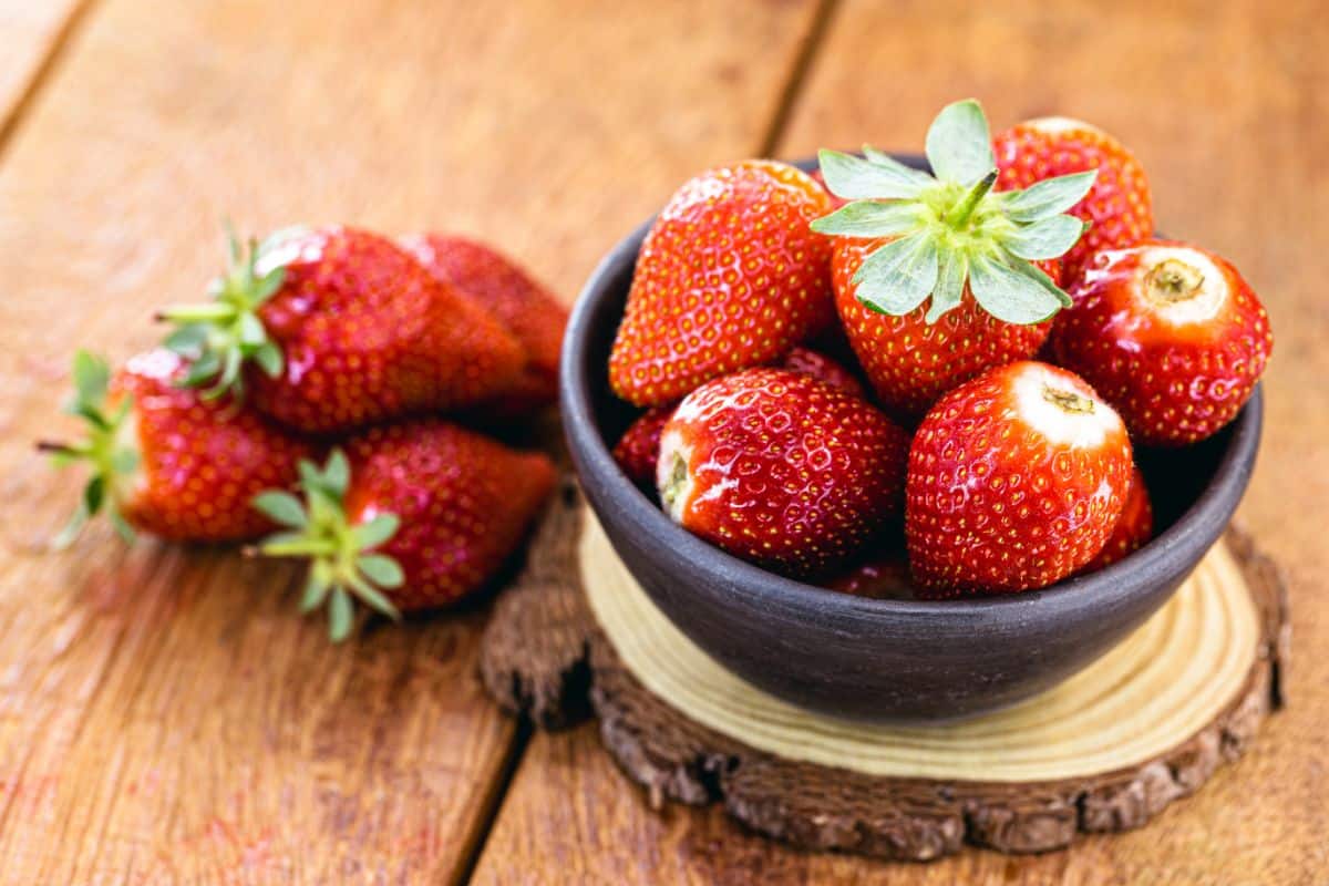 Bowl of ripe albion strawberries on a wooden table.