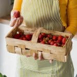 A woman holds a basket full of freshly picked strawberries in the kitchen.