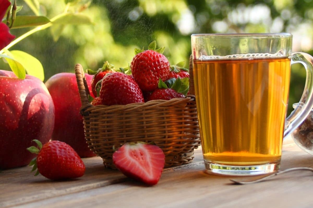 Wooden table with glass full of juice, basket full of strawberries and apples 