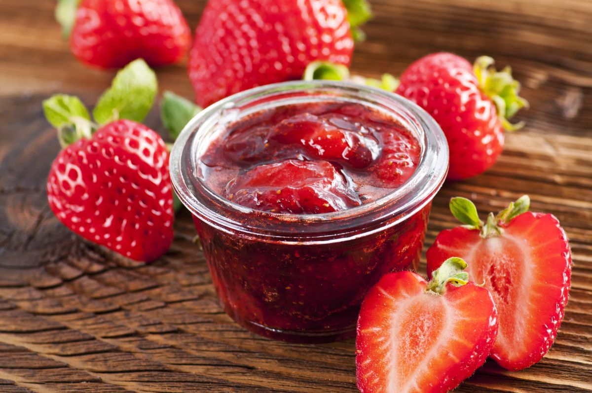 Strawberry jelly in plastic jar next to many strawberries round on table