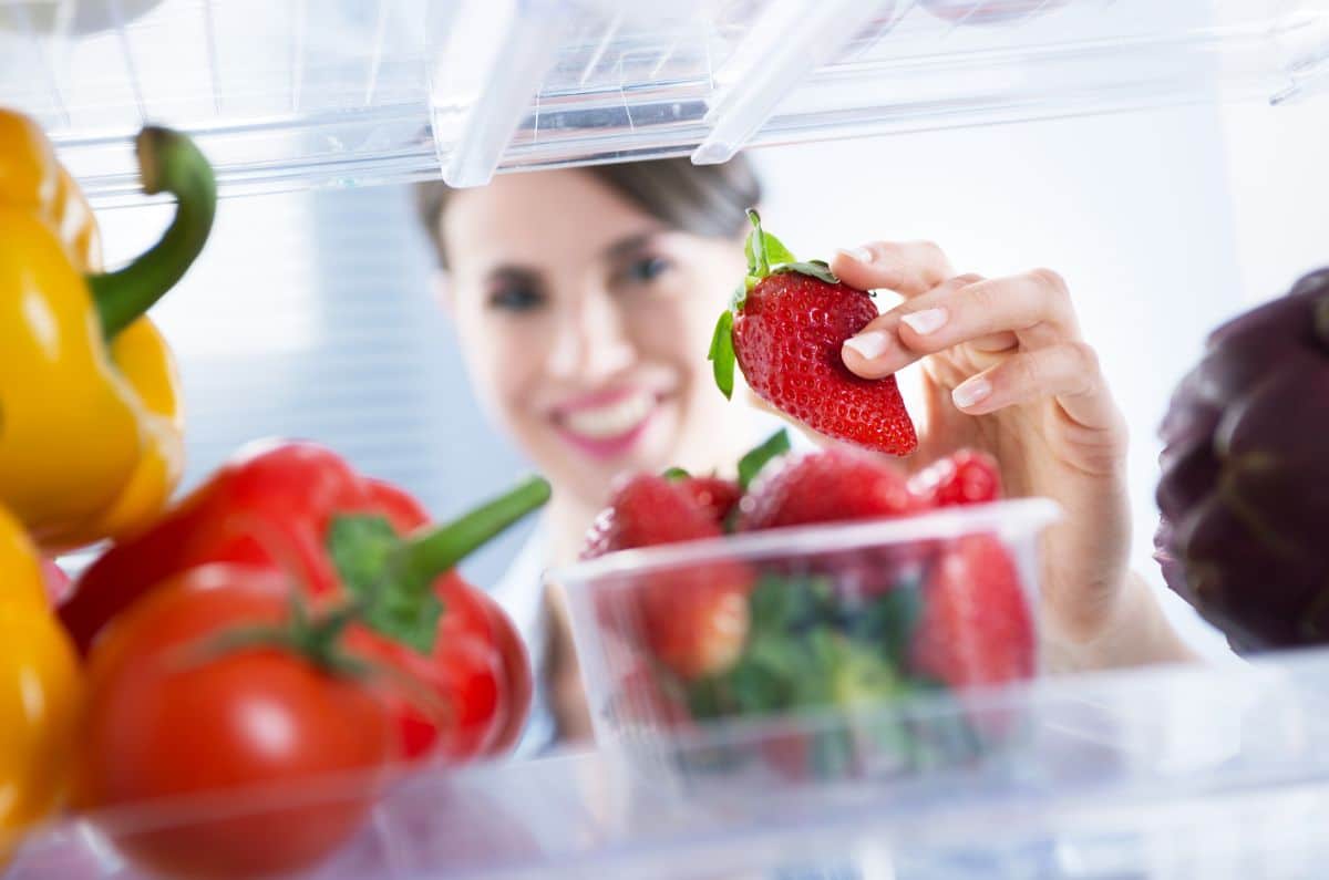 Woman picking up strawberry from refrigerator