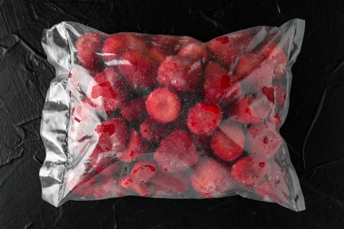 Fozen strawberries in plastic bag on black background