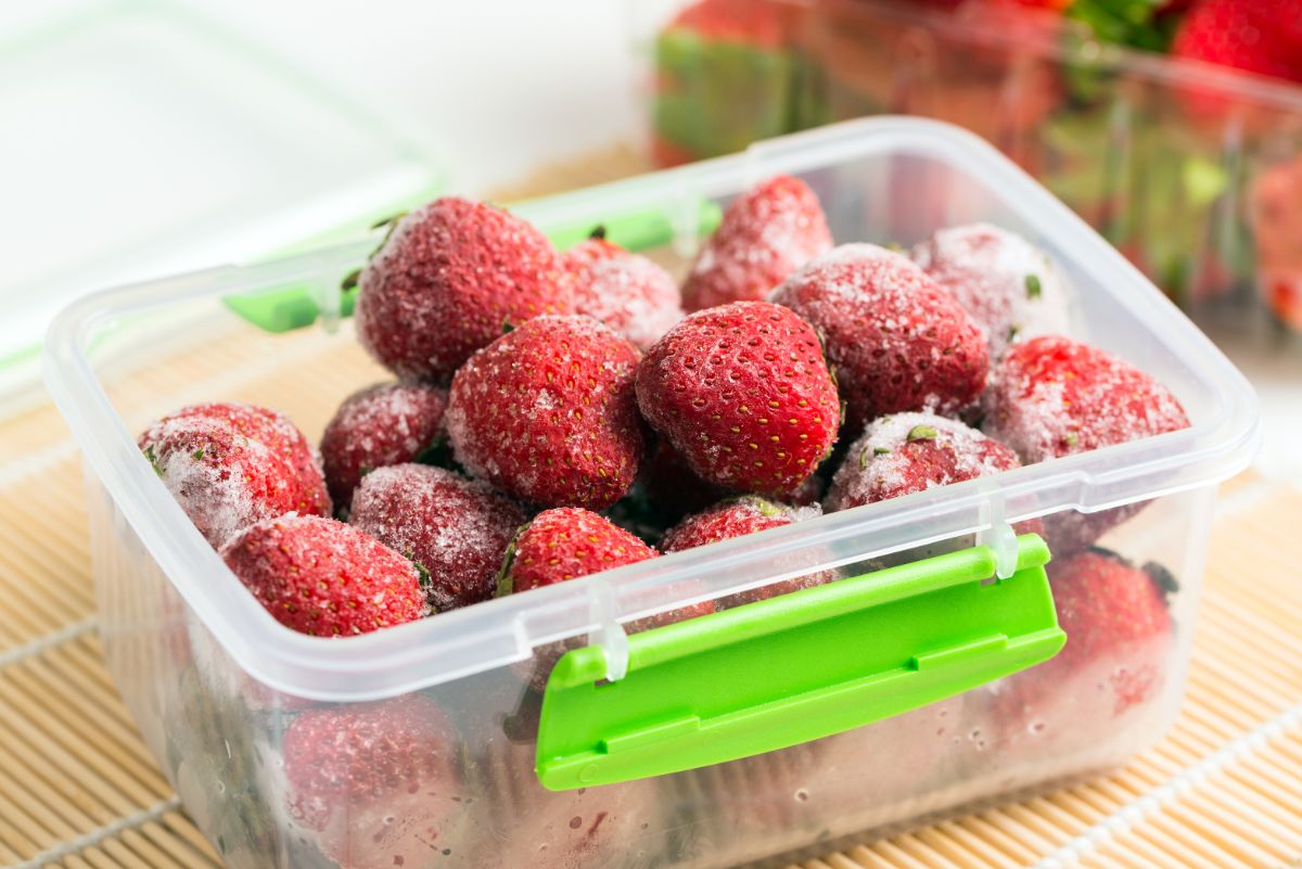 Frozen strawberries in plastic container on table