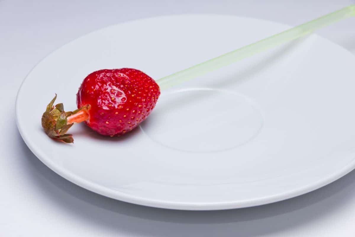 Strawberry penetrated by straw on white plate