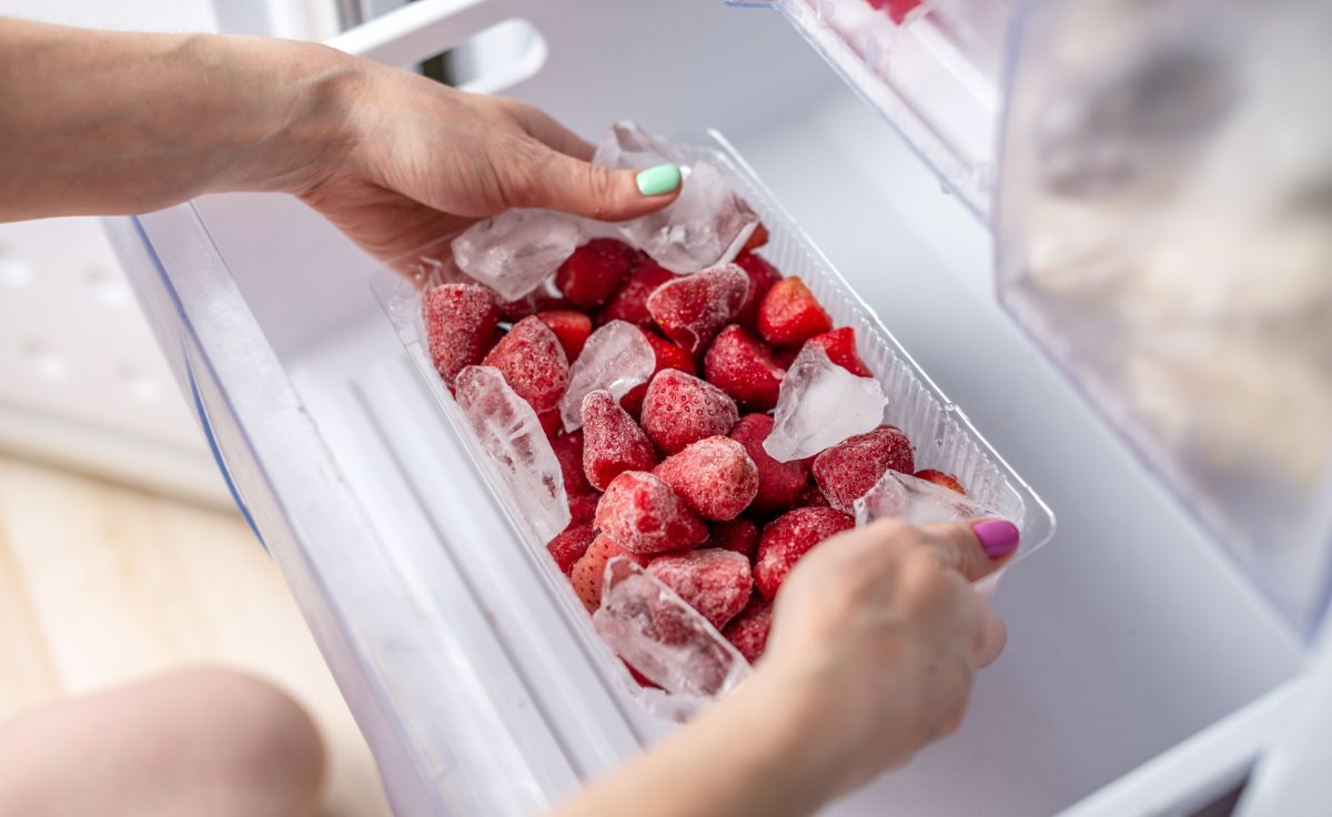 Hands holding box full of ripe strawberries and ice in freezer shelve