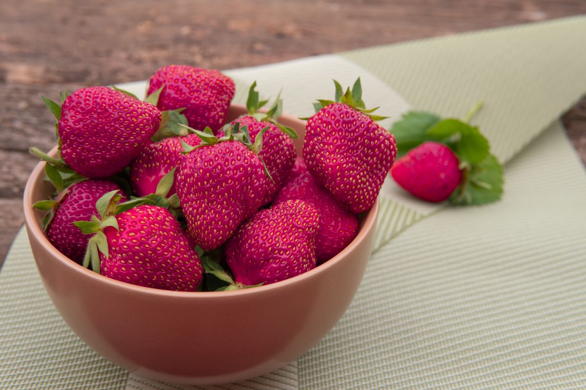 Purple fresh ripe strawberries in brown bowl