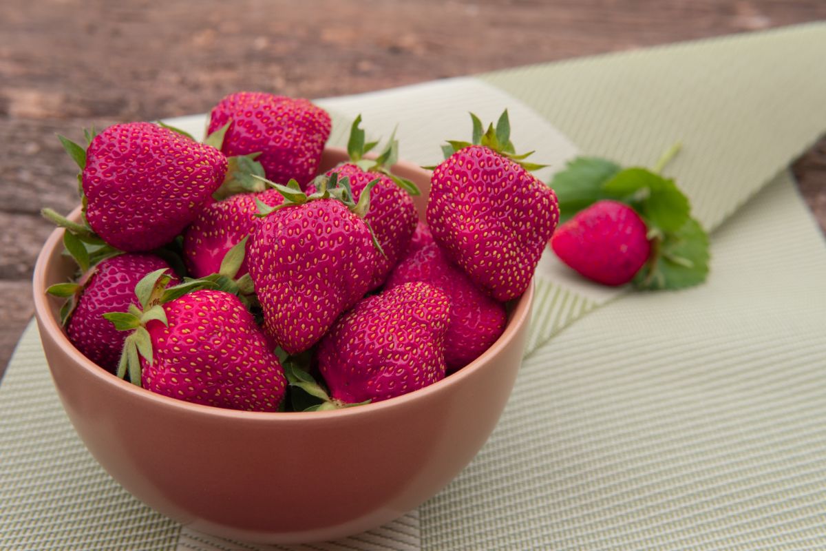 Puple strawberries in brown bowl on white foil