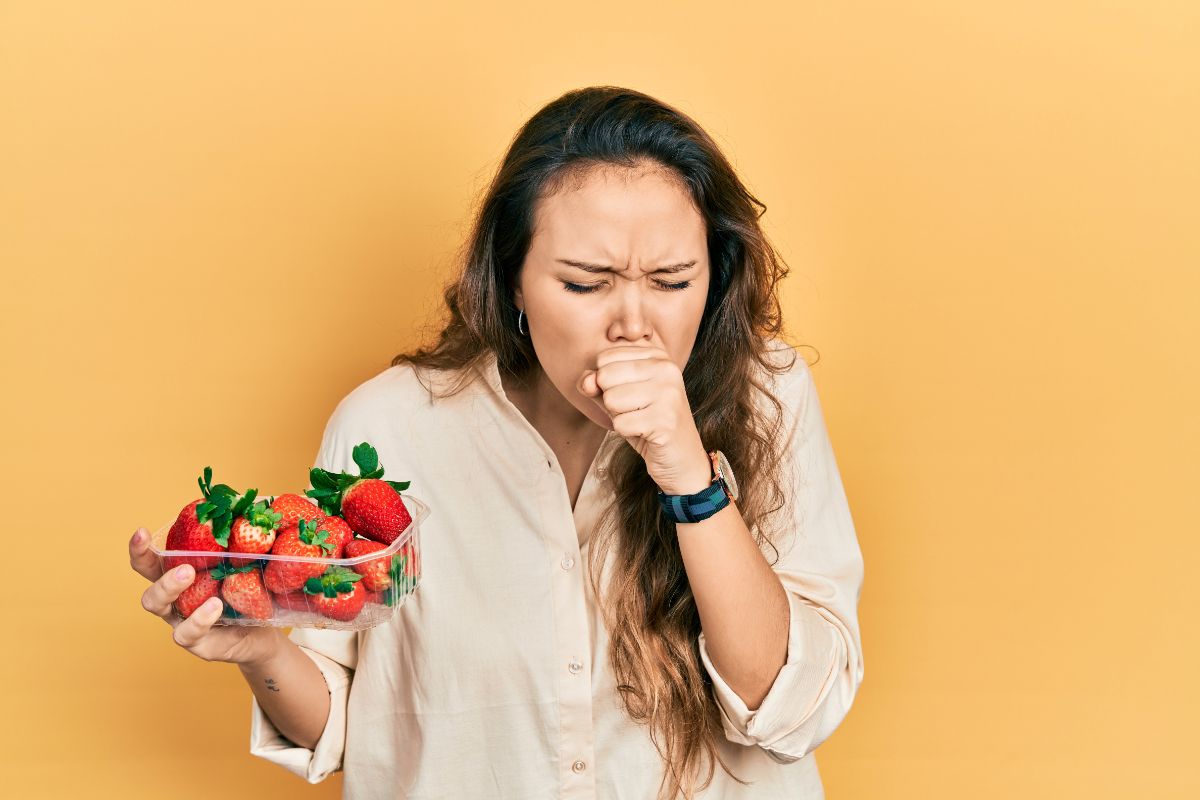 Coughing woman holdint container with strawberries on ligh brown background