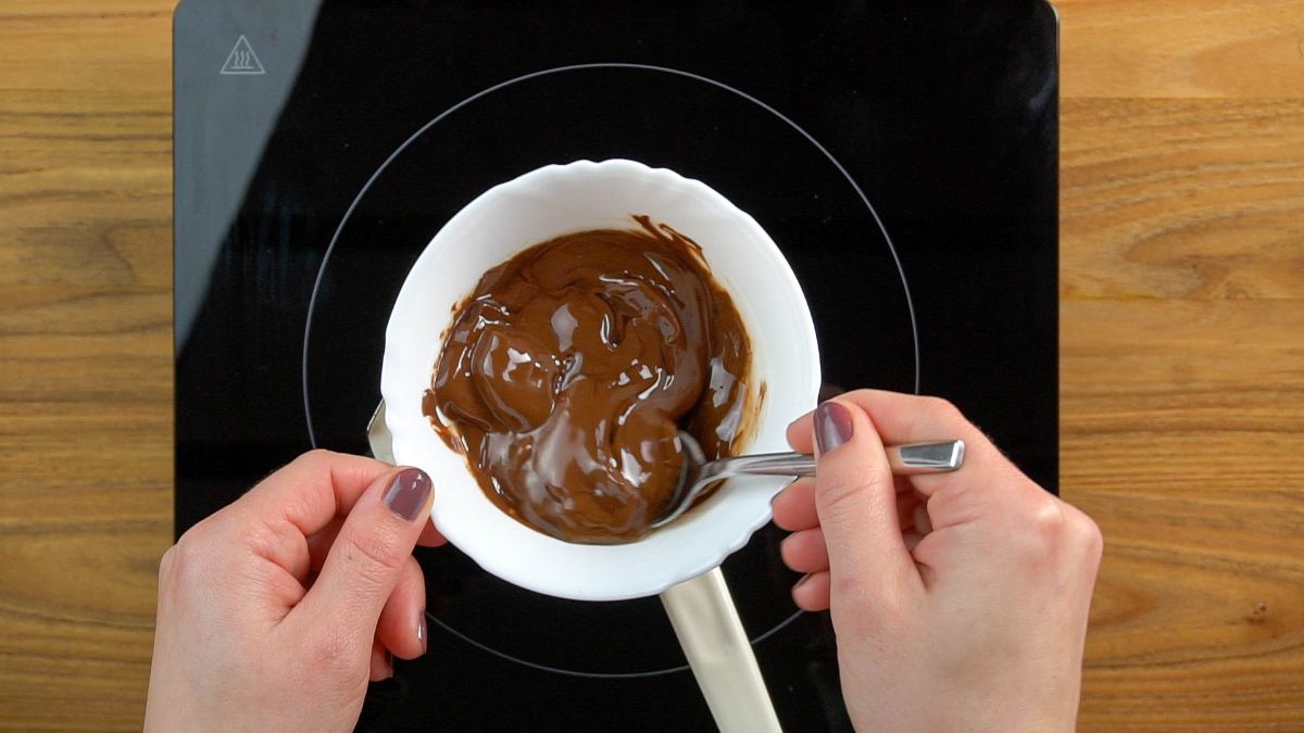 Hands stirring chocolate in a bowl on a stove.
