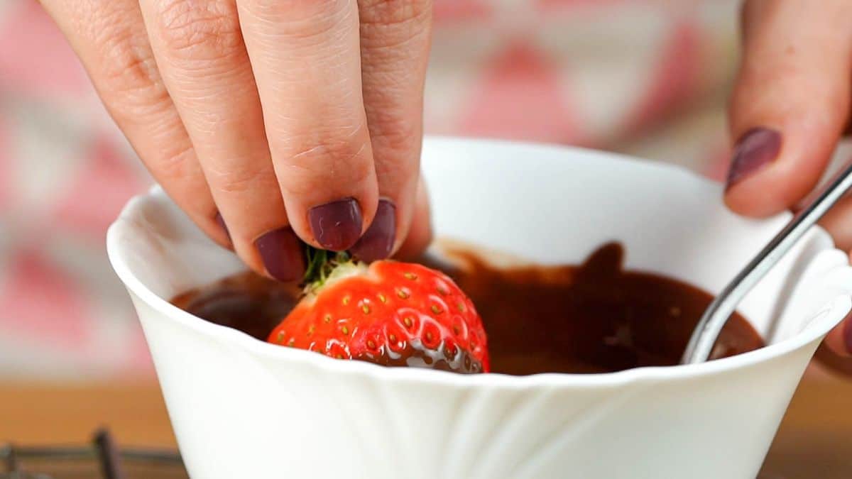 Hand diping a strawberry in a bowl of chocolate.
