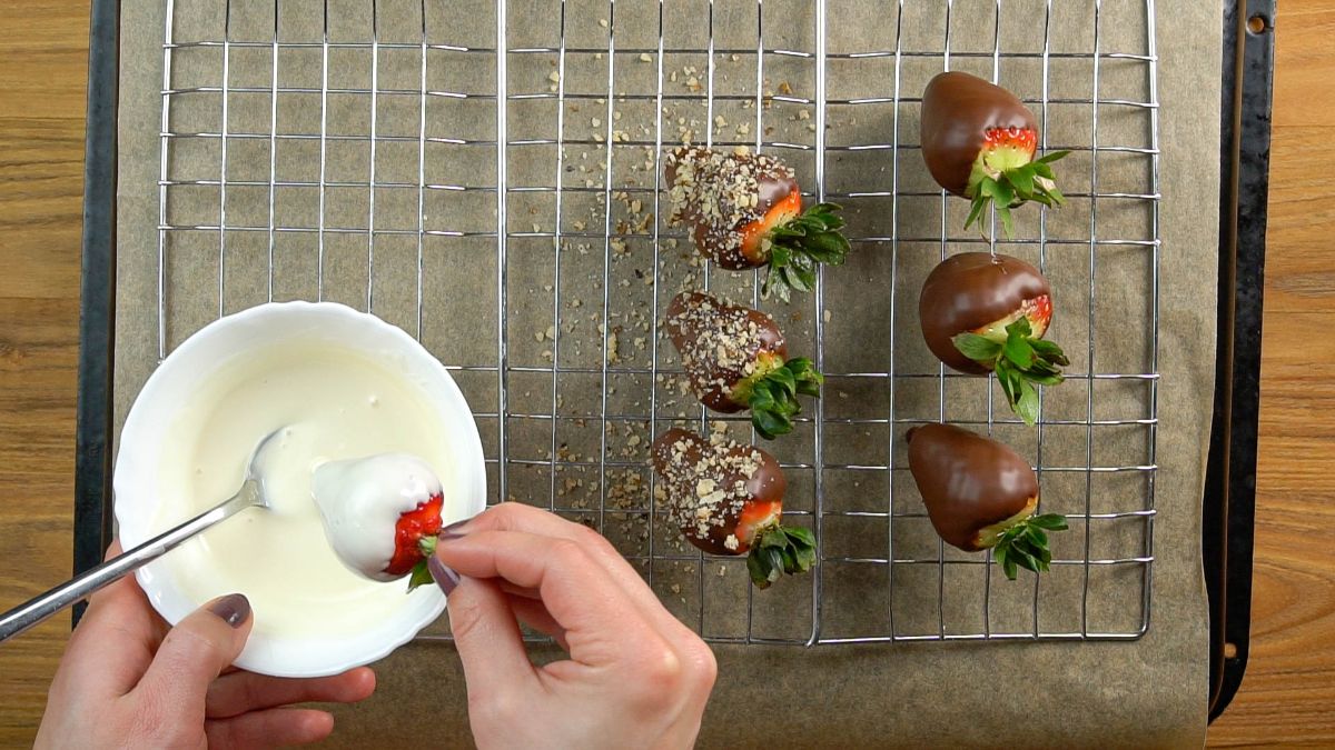 Hands holding a bowl of white chocolate and dipping a fresh ripe strawberry.
