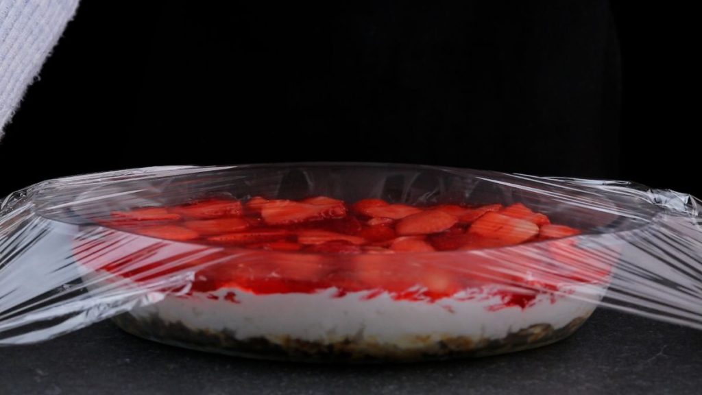 Strawberry pretzel salad in glass container covered by plastic foil.