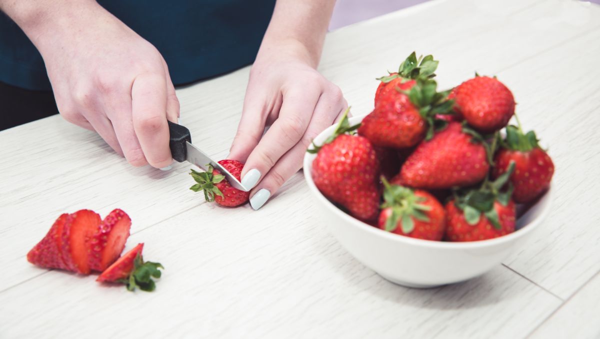 A person cutting a top off a strawberry