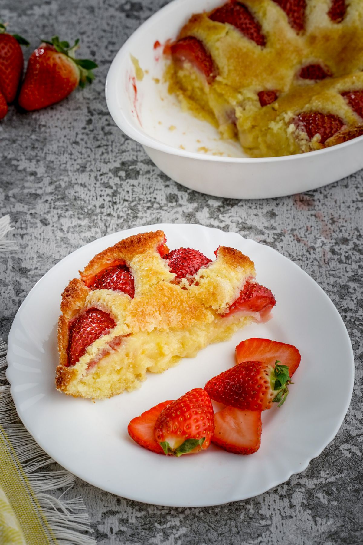 Piece of fresh strawberry cake on a white plate with sliced strawberries.