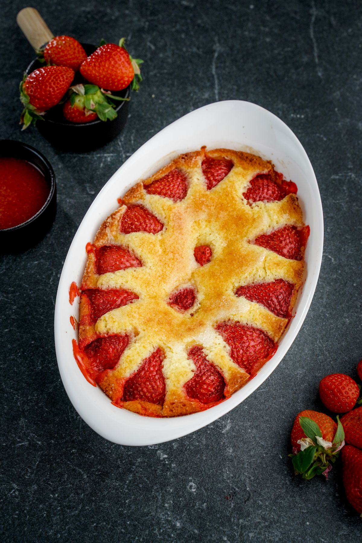 Fresh strawberry cake in a white baking pot on a table with ripe strawberries around.