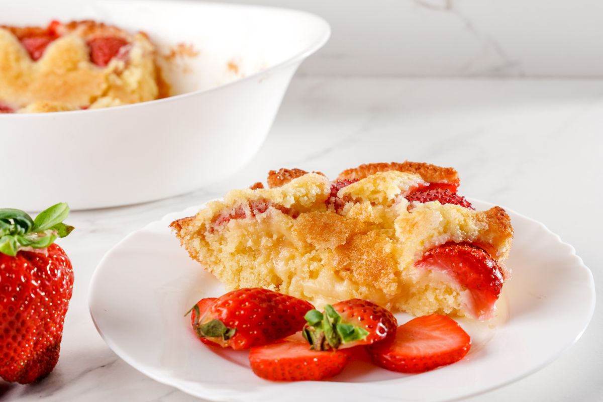 Piece of a strawberry cake on a white plate with sliced strawberries,