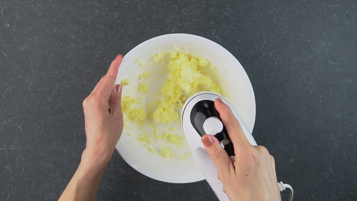 Hands mixxing ingredients with an electic mixxer  in a bowl.