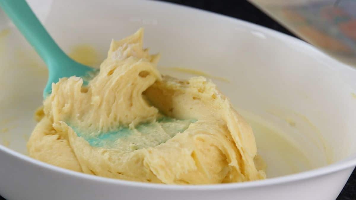 cake dough in a white baking pot and a blue spatula.