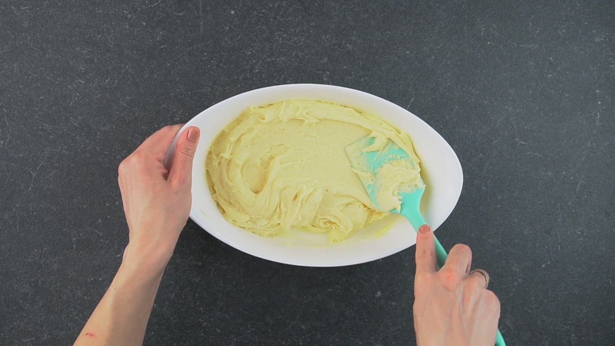 Hands spreading a cake dough with a spatula in a baking pot.
