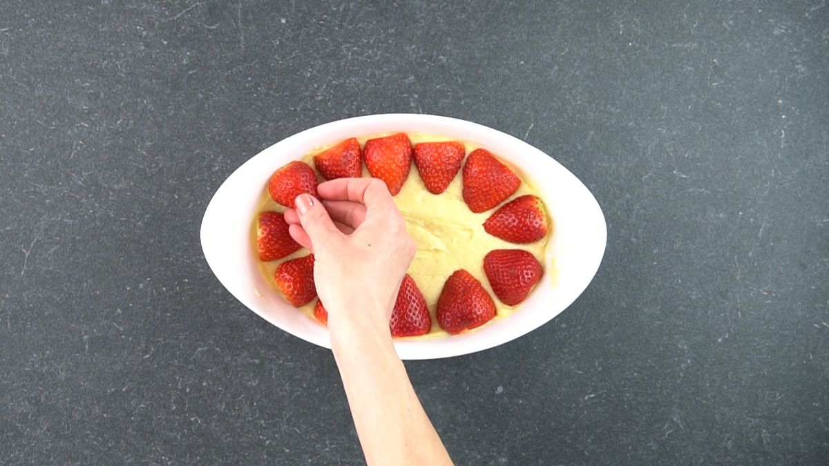 Hand placing sliced strawberries on a cake dough.