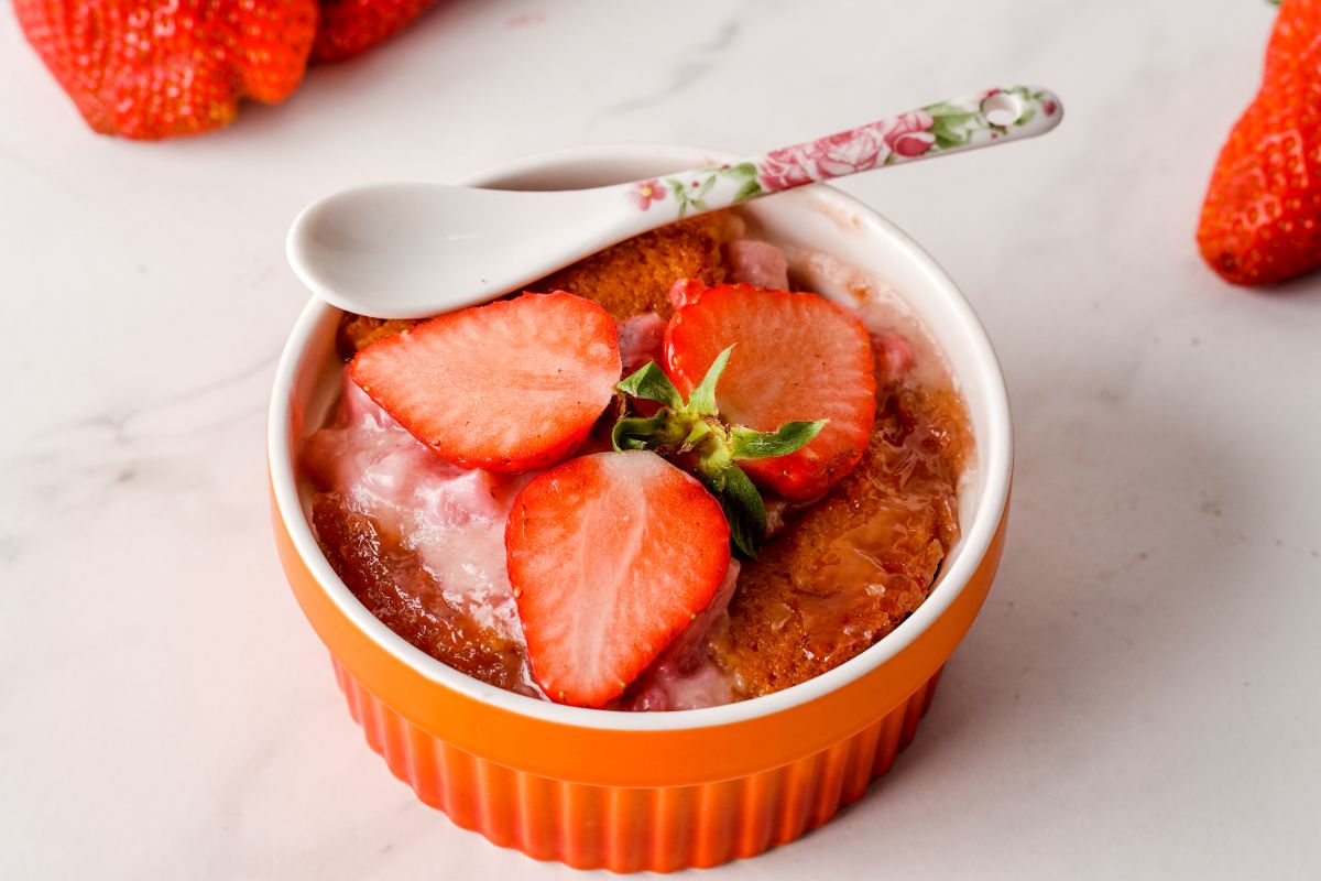 Fresh strawberry cobbler in a small bowl with a spoon and sliced strawberries.