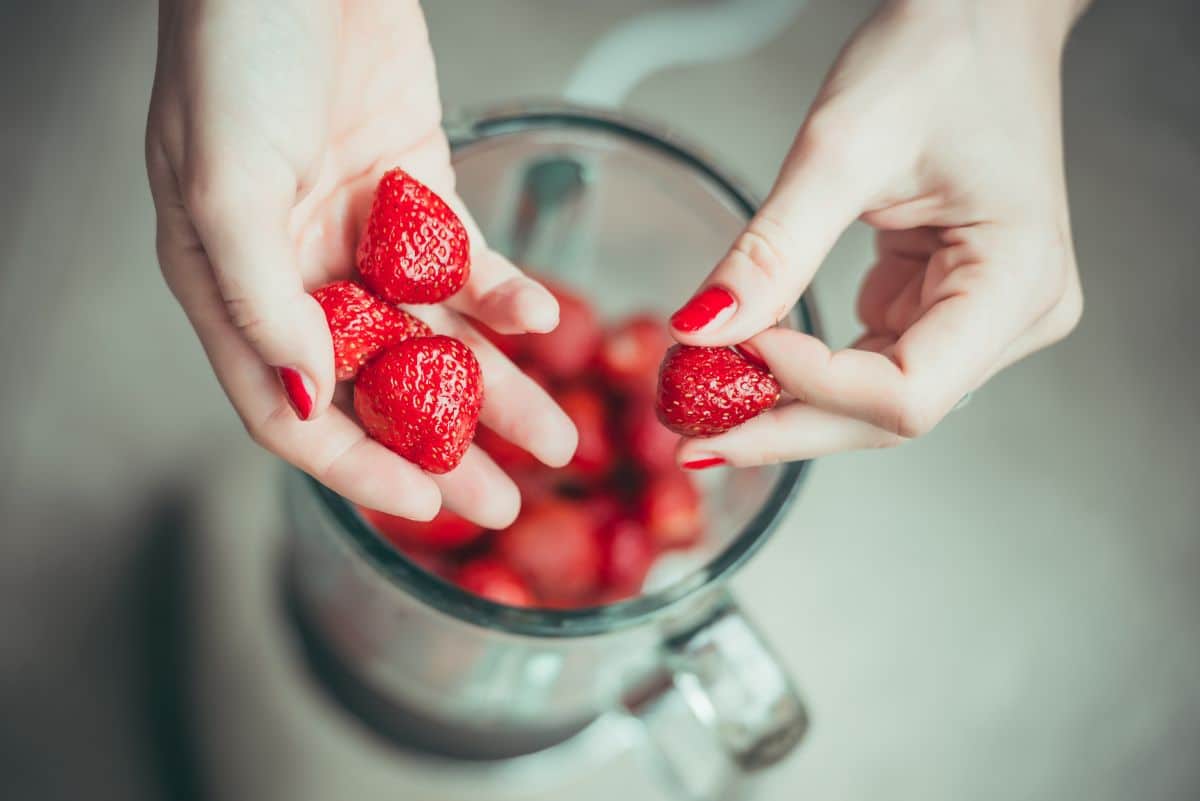 Hands putting strawberries into a blender.