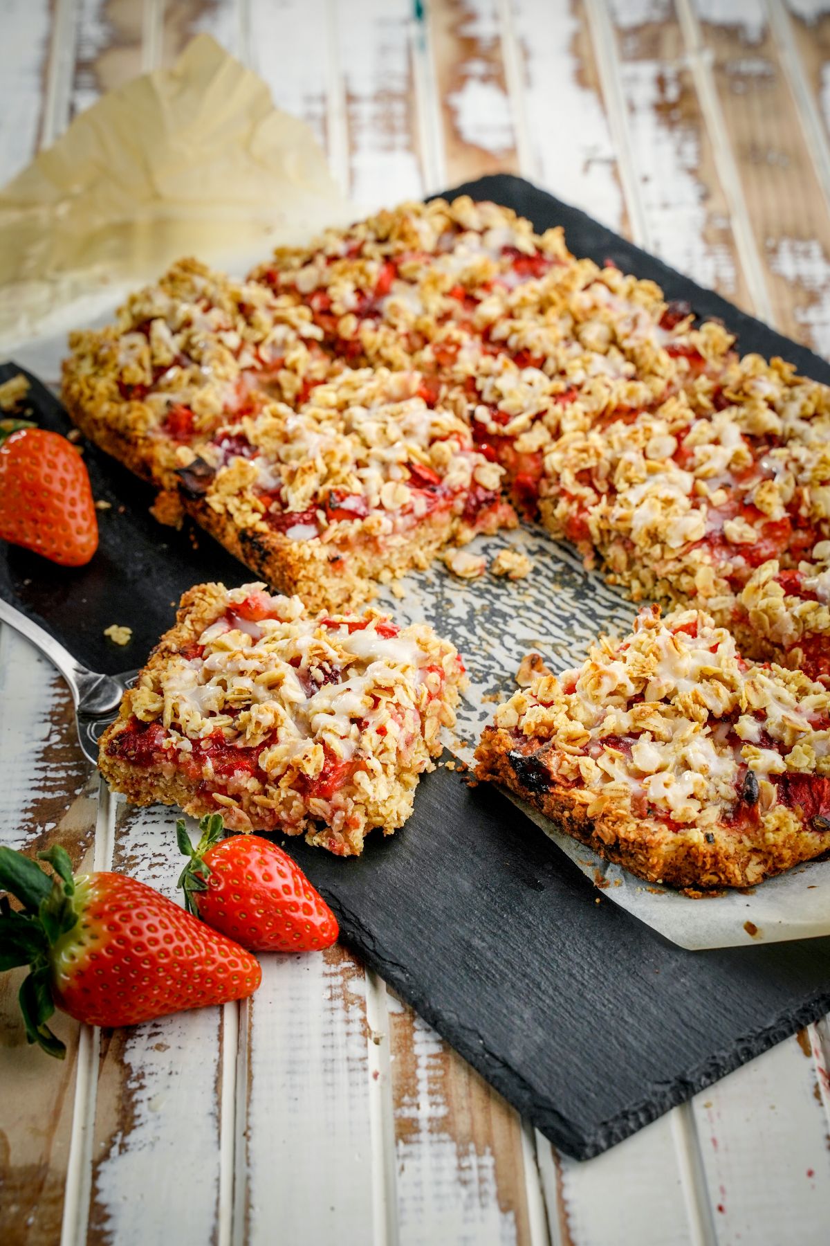 Baking tray full of healthy strawberry oatmeal bars with ripe strawberries on a table.