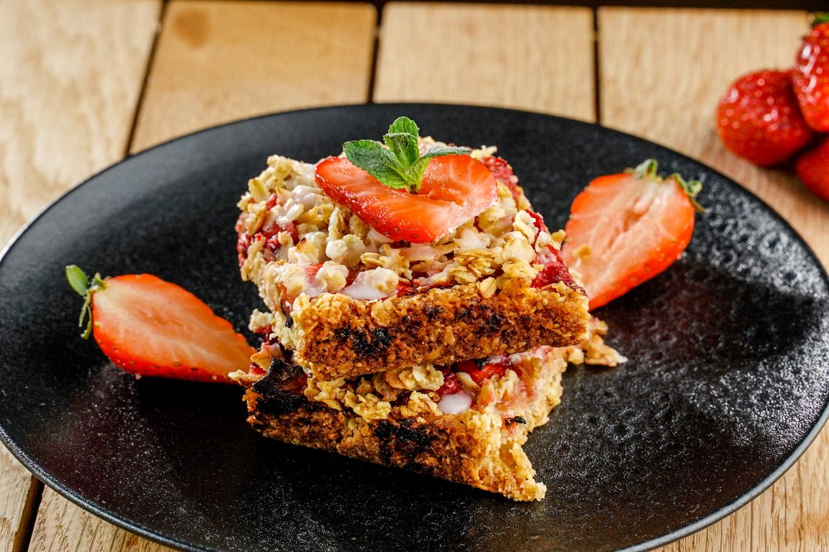 Healthy strawberry oatmeal bars on a black tray with sliced strawberries.