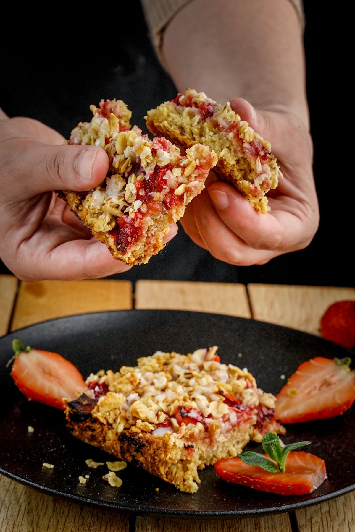 Hands holding healthy strawberry oatmeal bars over a tray with strawberry bar.