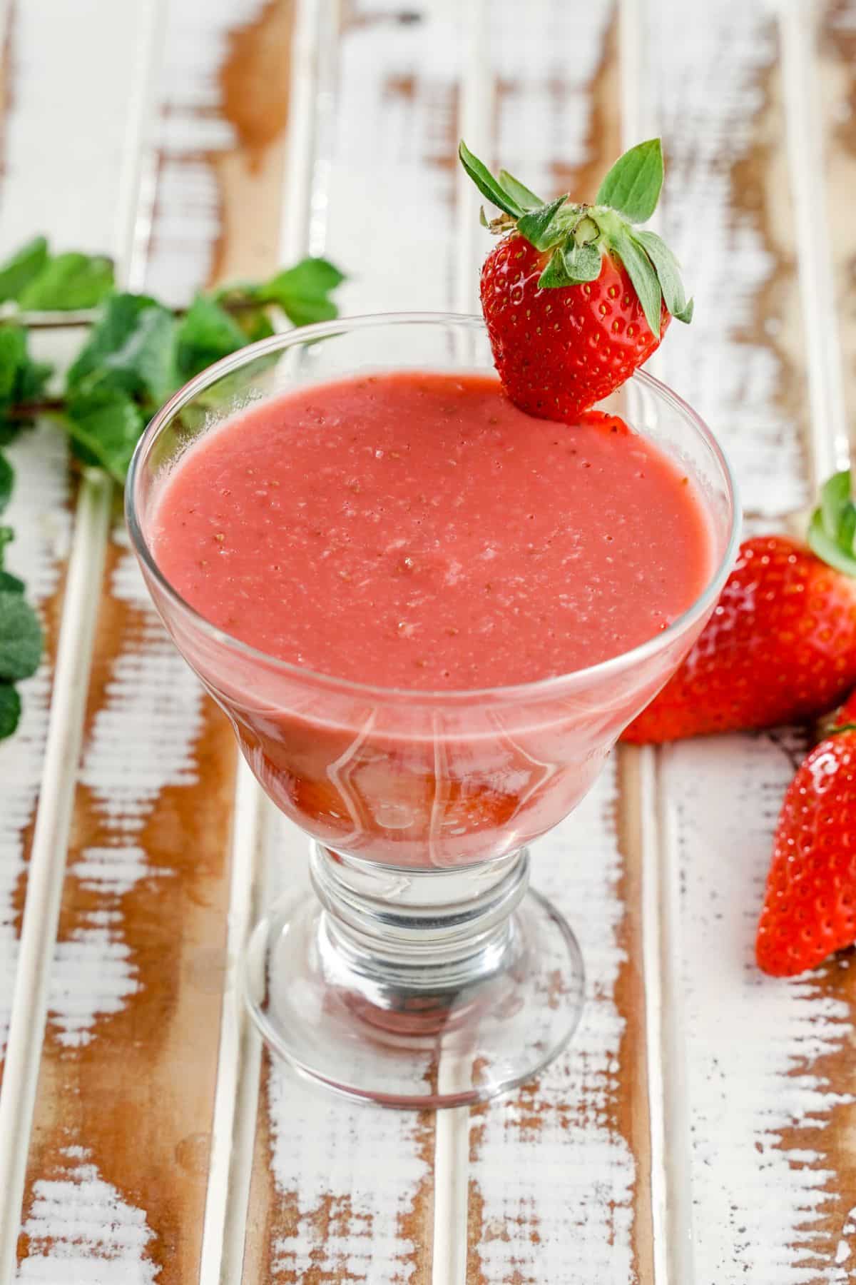 Tall glass full of homemade strawberry pudding with ripe strawberries on a table.