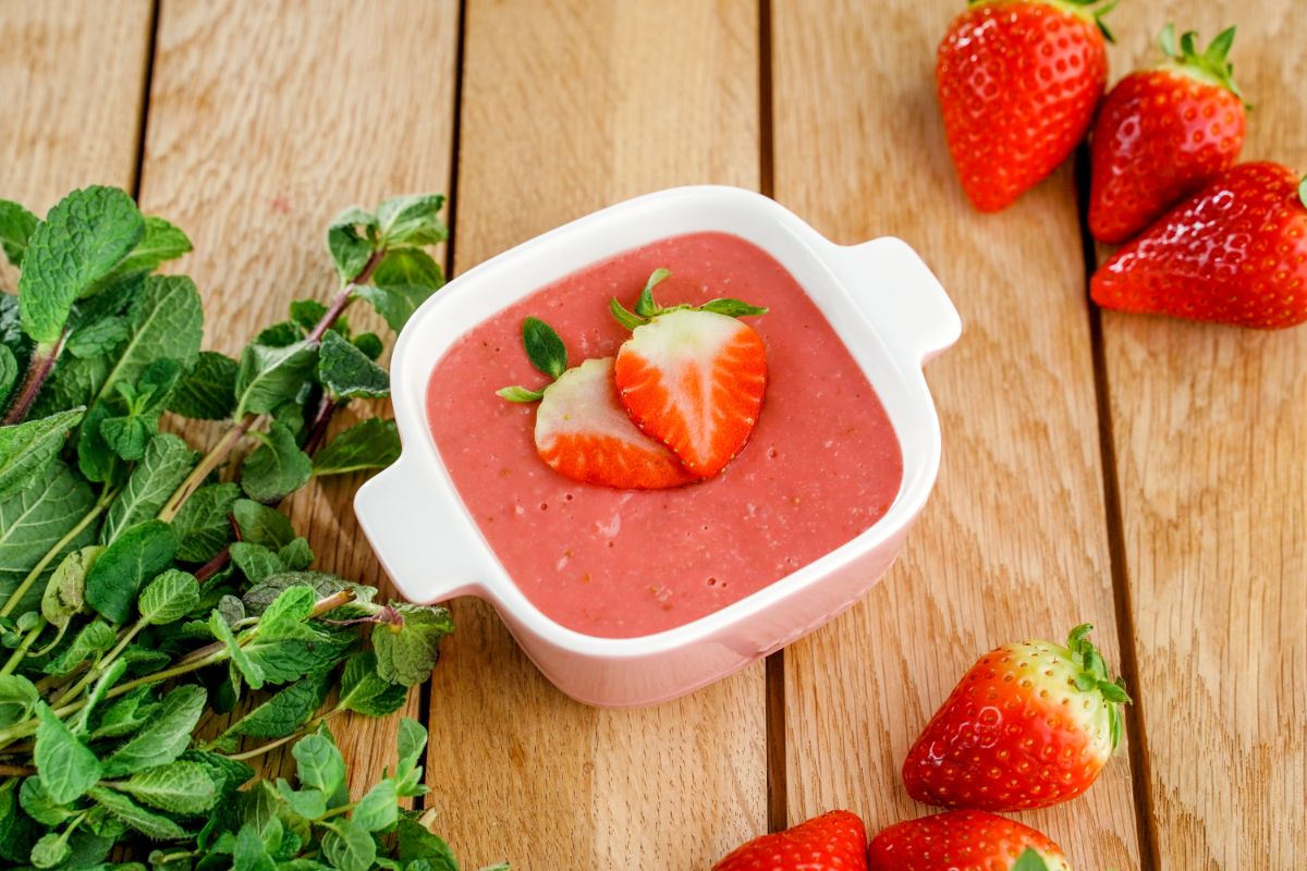 Bowl of homemade strawberry pudding on a table with ripe strawberries around.