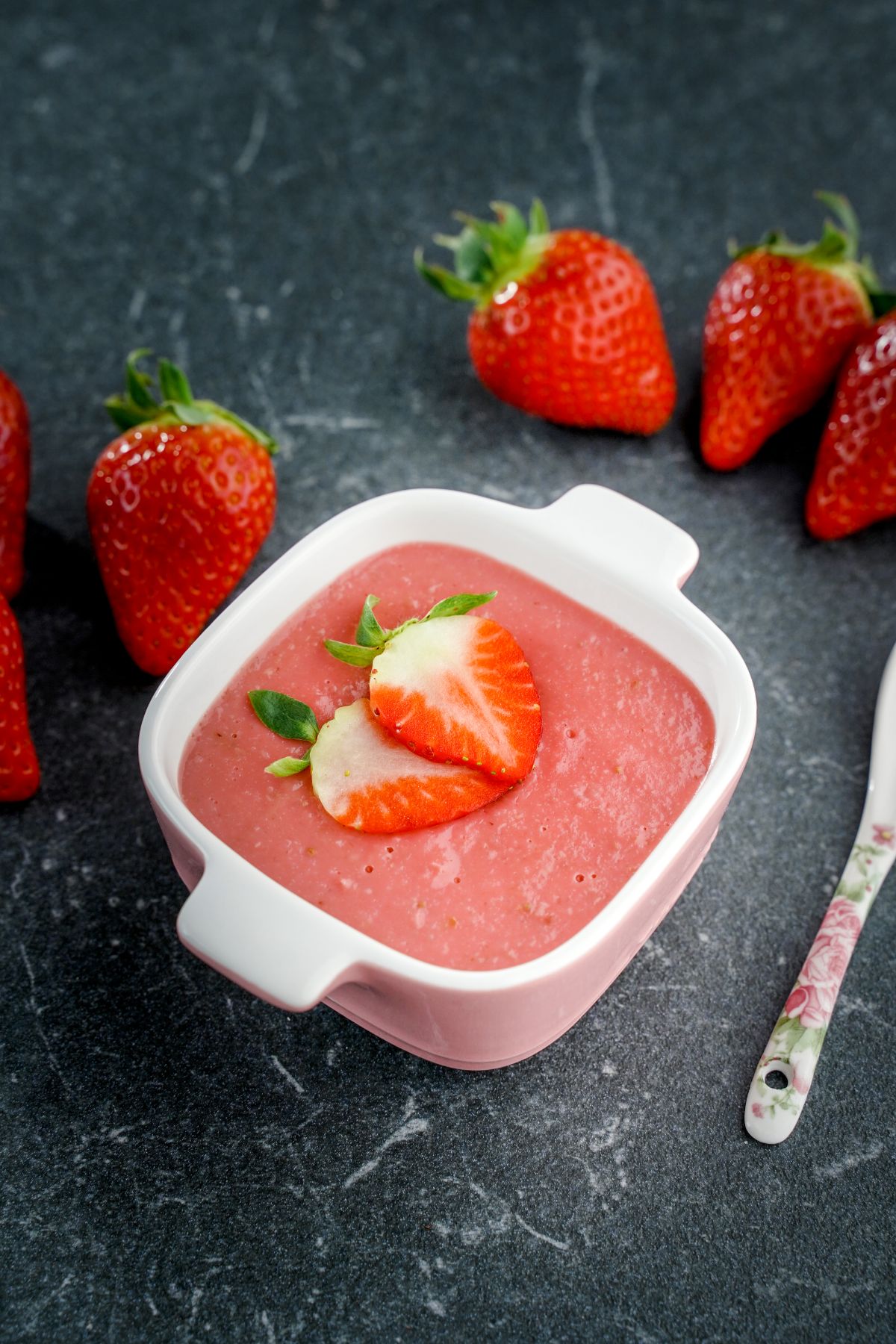 Bowl of homemade strawberry pudding with sliced strawberries and with ripe strawberries around.