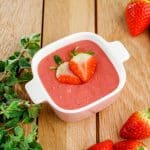 Bowl of homemade strawberry pudding on a table with ripe strawberries around.