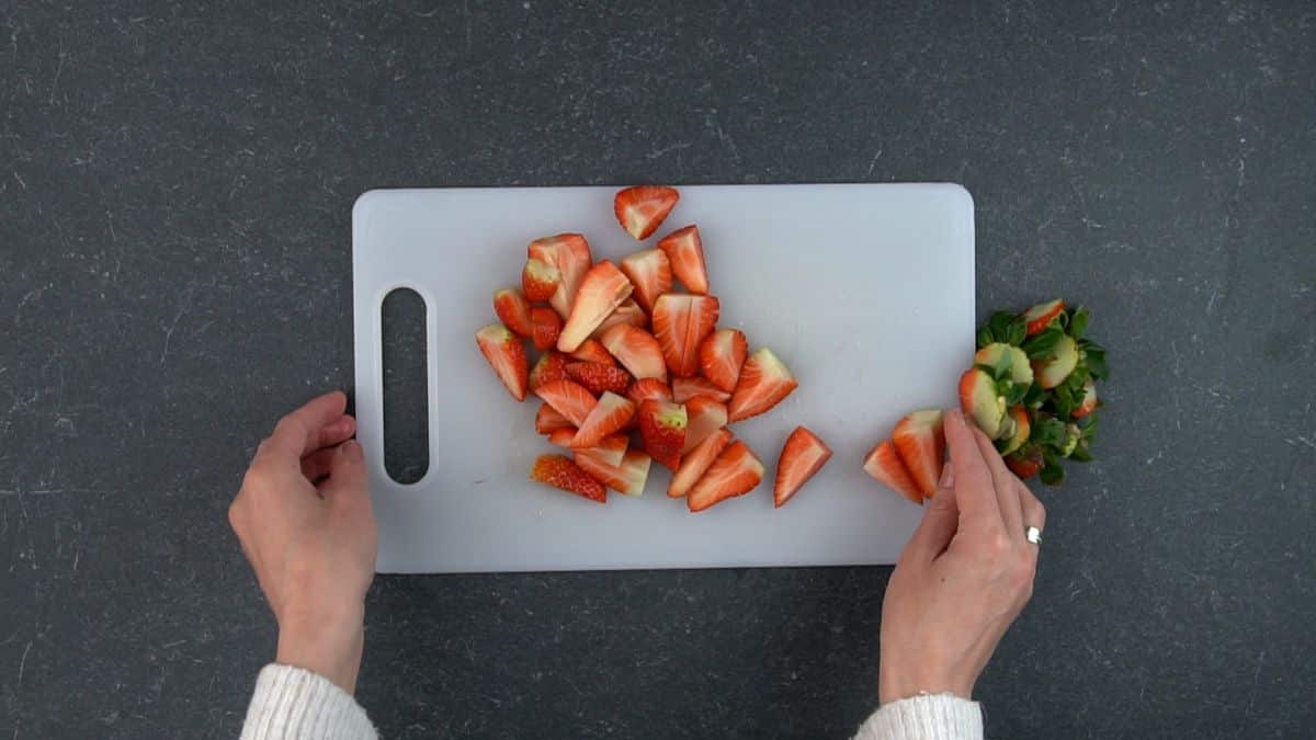 Hands cutting ripe strawberries on a cutting board.