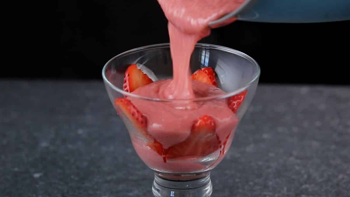 Pouring a strawberry pudding into a tall glass with strawberries,