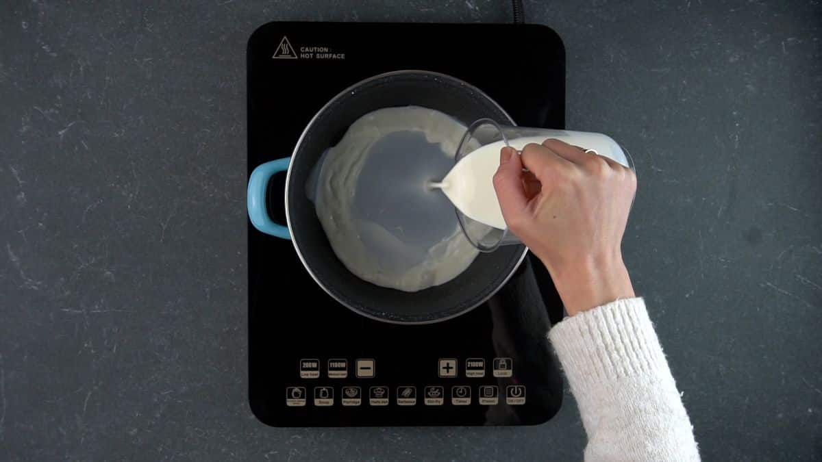 Hand pouring a milk into pot on a stove.