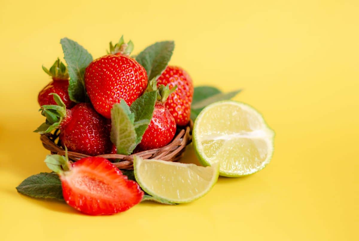 Fresh sripe strawberries with sliced lemon on yellow background