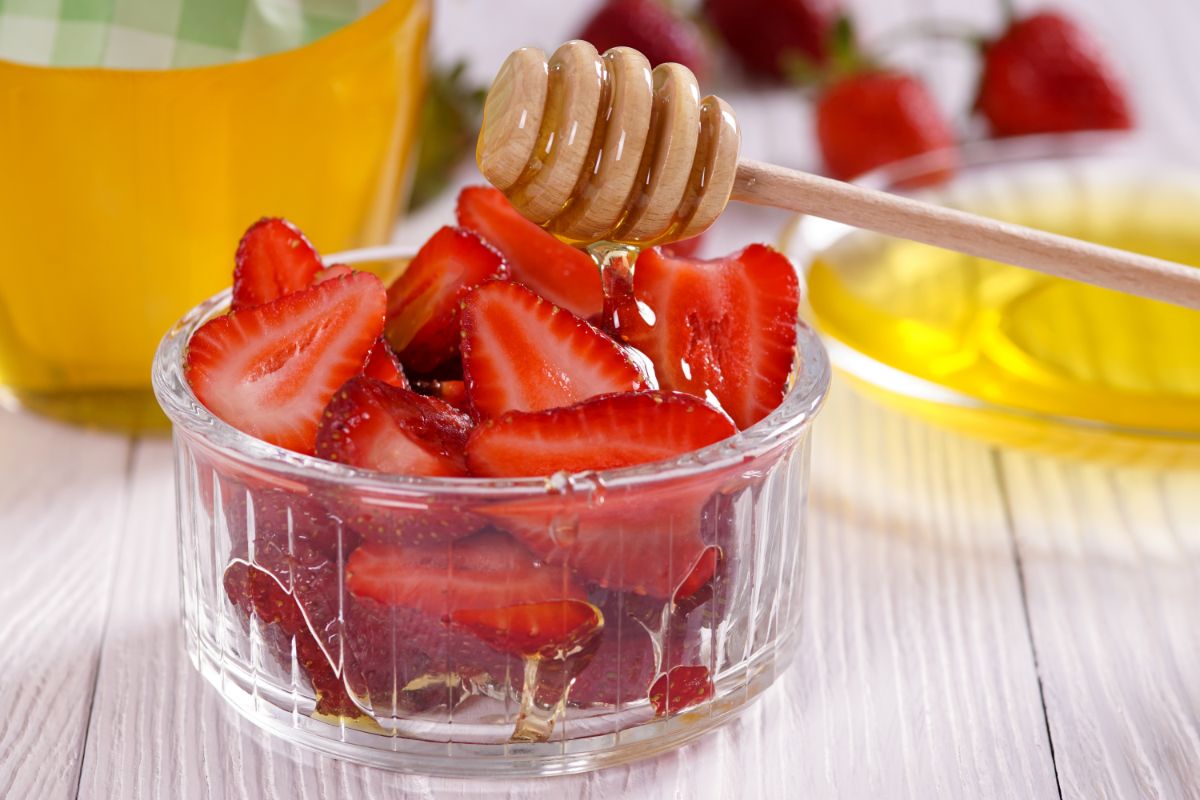 Sliced strawberries in container with honey