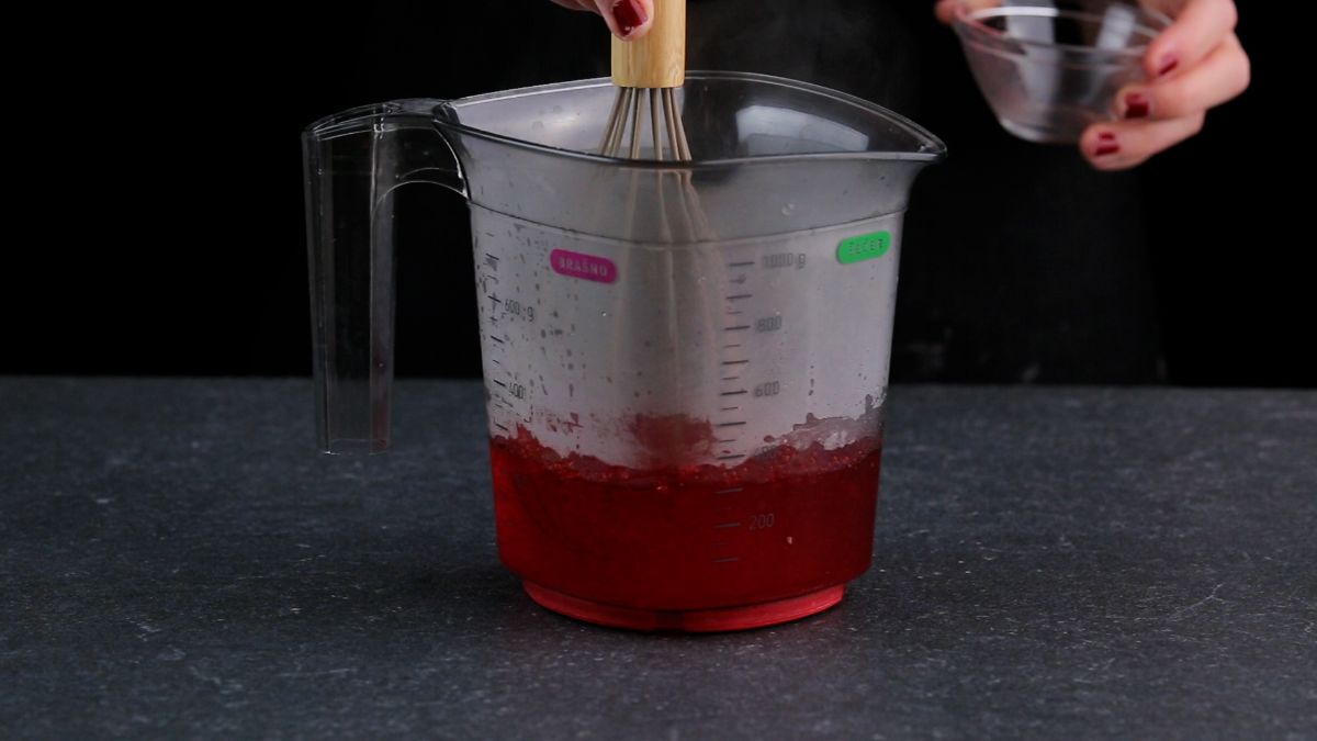 Mixxing strawberry jello in a container.