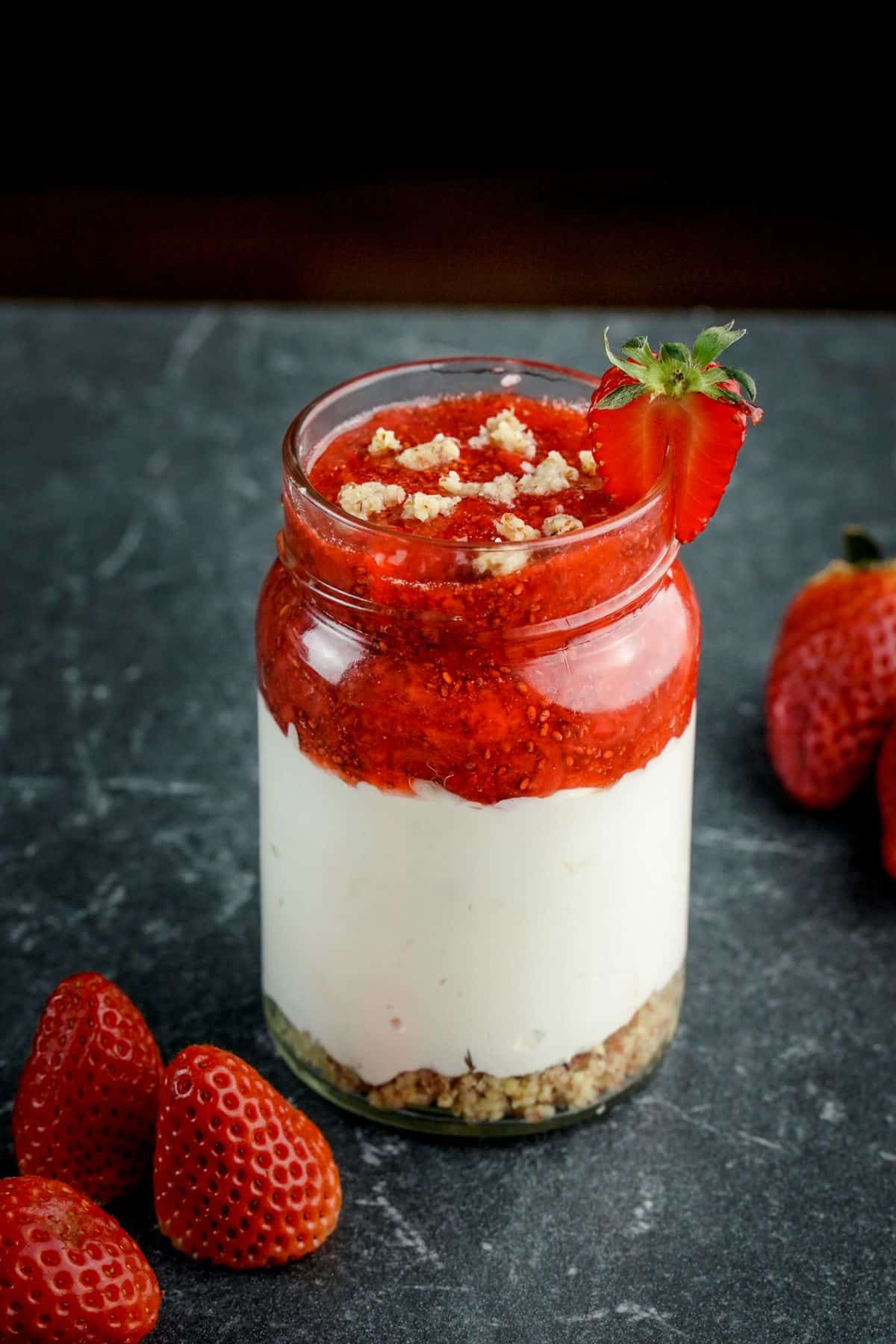 A close-§up of a No Bake Keto Strawberry Cheesecake Jar on a gray table next to ripe strawberries.