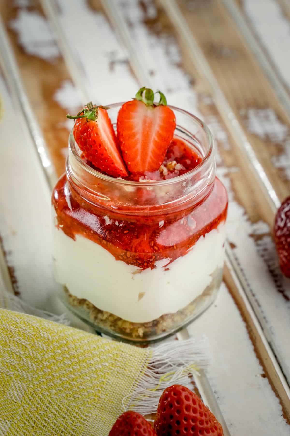 A close-up of a No Bake Keto Strawberry Cheesecake Jar on a wooden table.