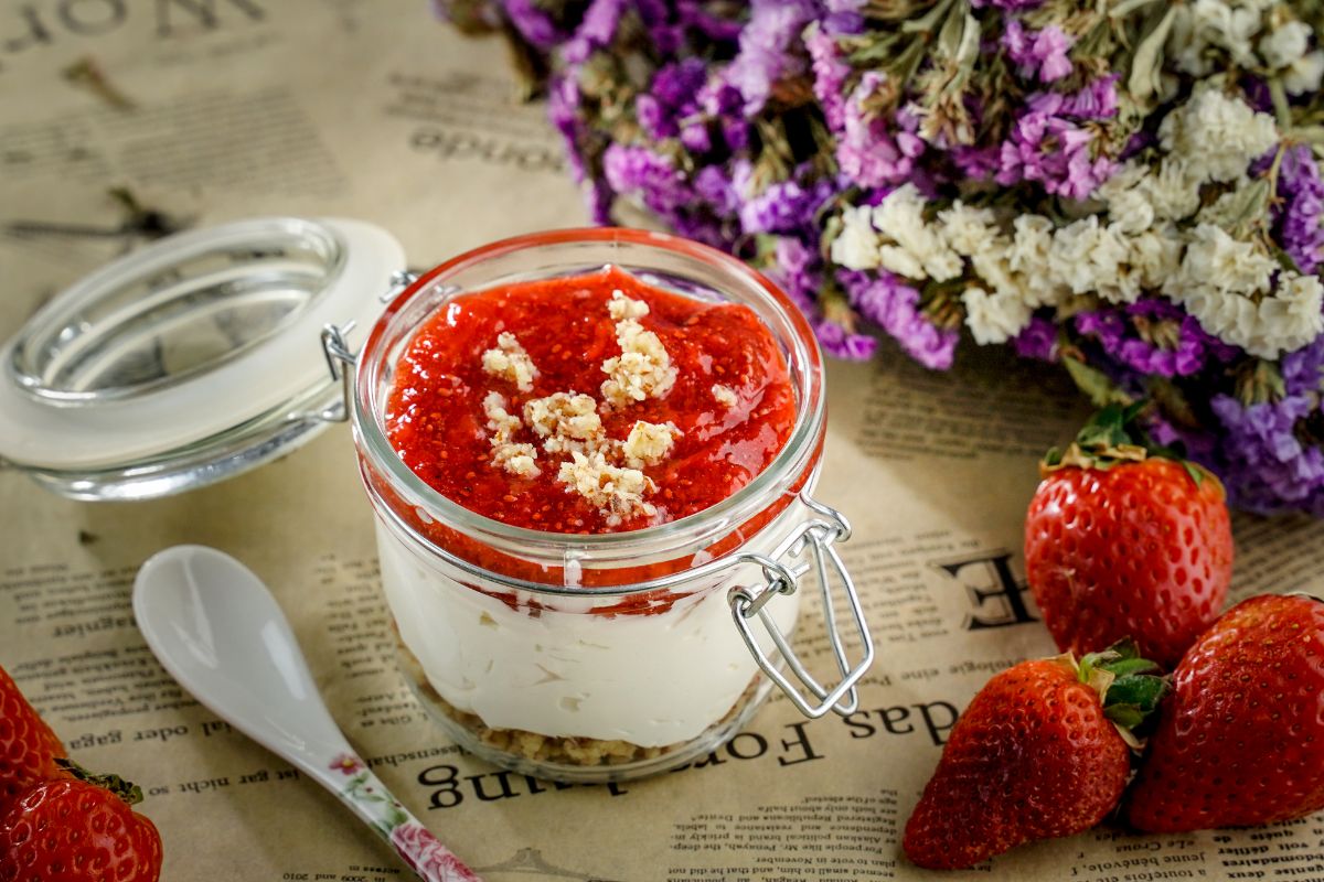 A No Bake Keto Strawberry Cheesecake Jar on a table next to a spoon, ripe strawberries and bouquet of flowers.