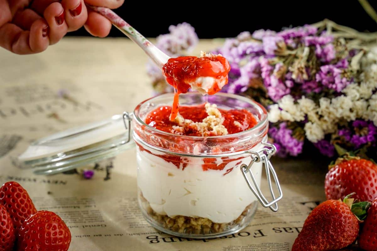 A hand with a spoon scooping a No Bake Keto Strawberry Cheesecake Jar on a table.