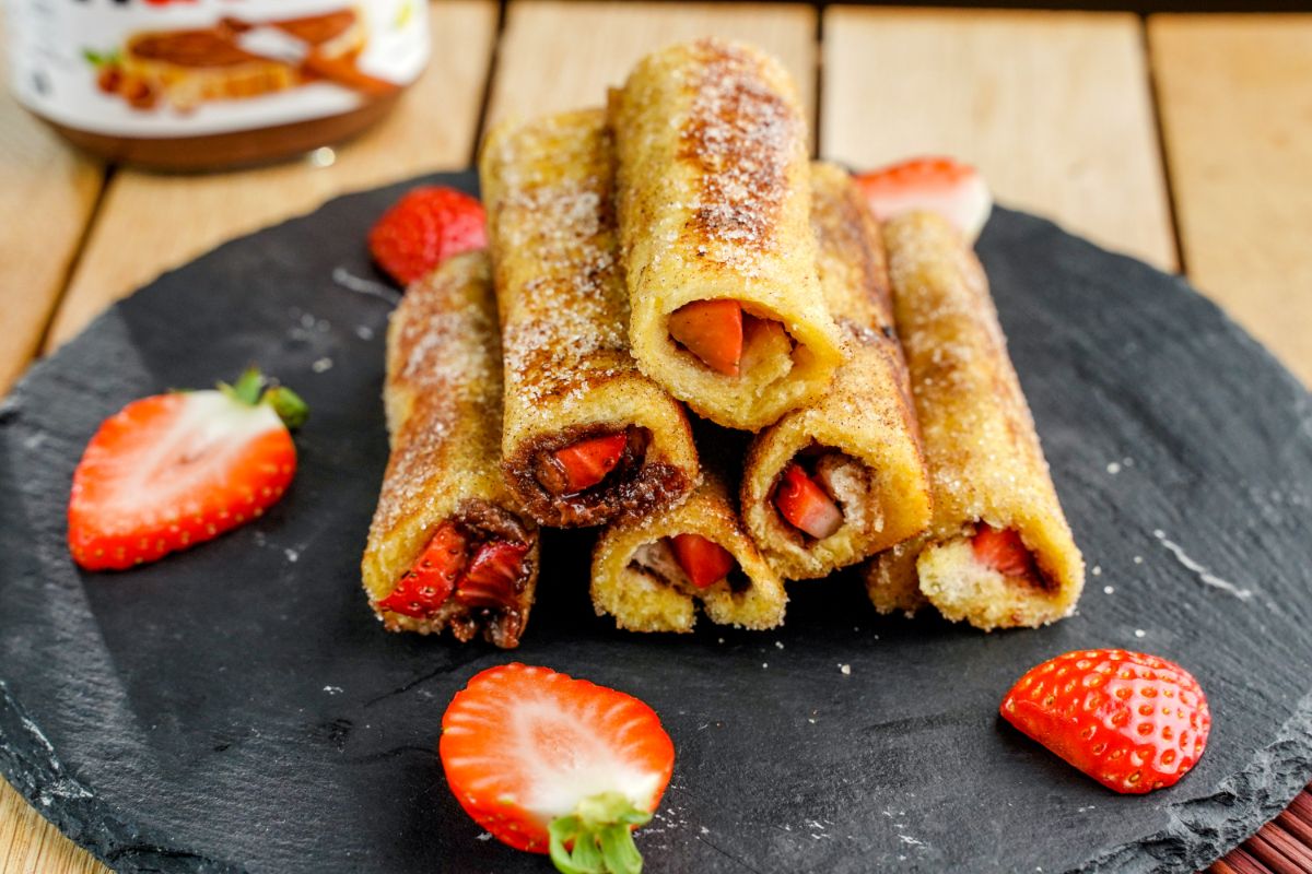 Nutella Strawberry Rolled French Toasts on a black tray with sliced strawberries around.