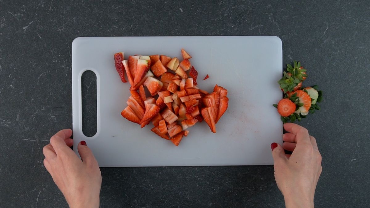 Hands holding a cutting board with sliced strawberries.