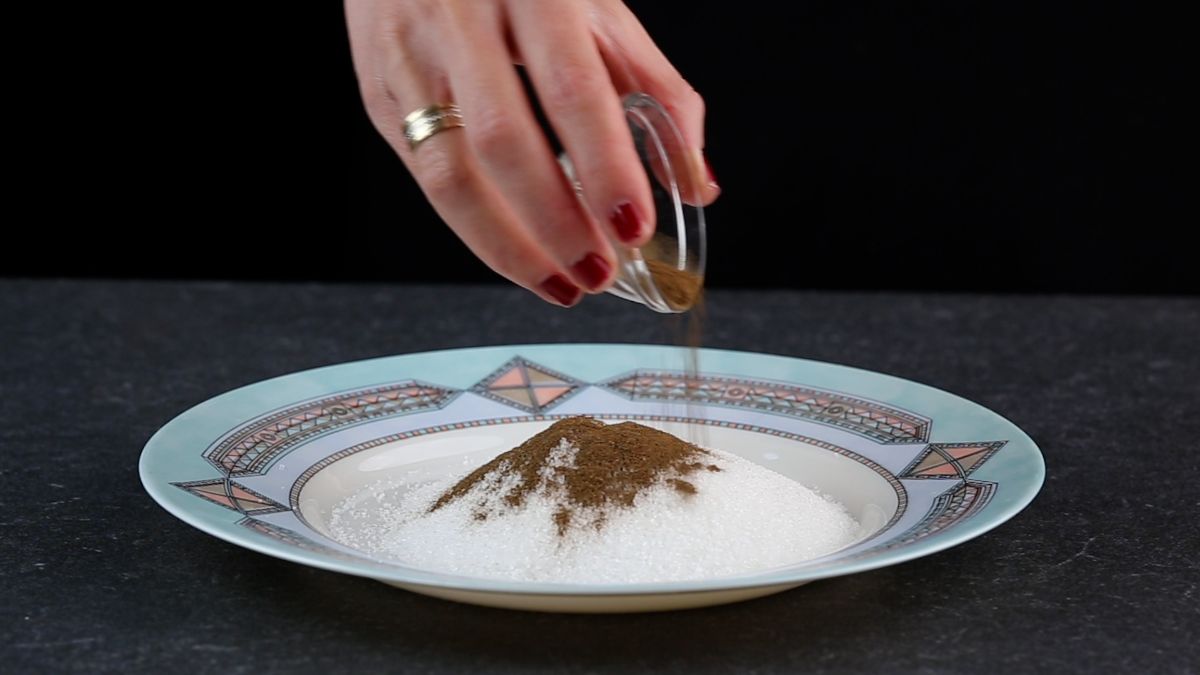 A han adding cinnamon in a bowl on a plate with sugar.