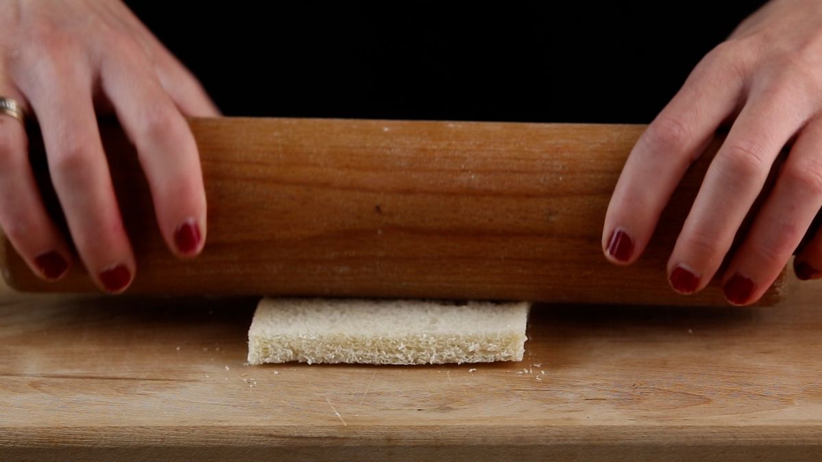 Hands rolling a bread with a wooden roller.