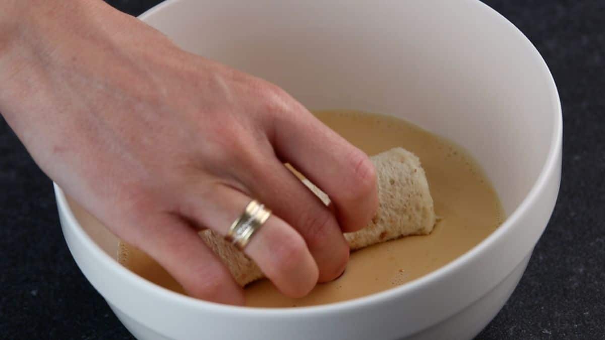 A hand dipping a rolled piece of bread in a mixture in a bowl.