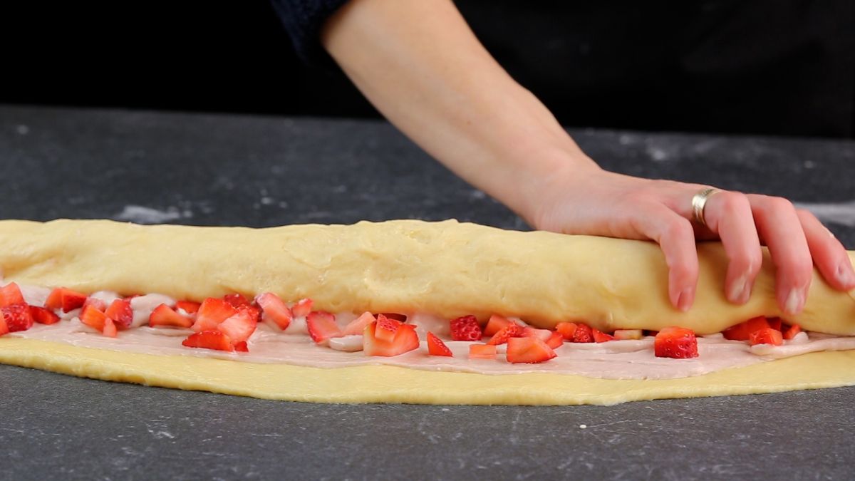 A hand rolling a dough on a table.