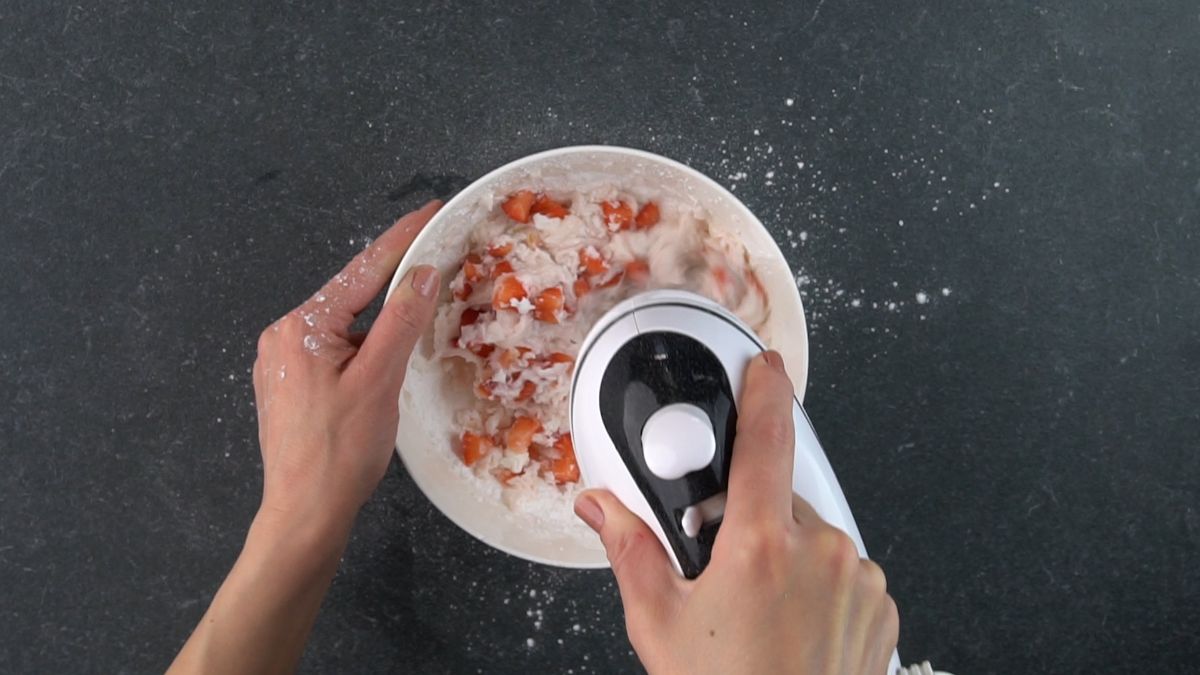 Hands mixxing with an electric mixxer ingredients in a white bowl.